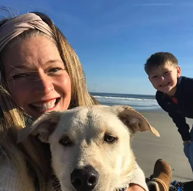 smiling woman with a child and a dog on the beach